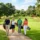 Quatre golfeurs d’affaires adultes marchant ensemble sur le parcours, sac de golf à l’épaule, discutant sous un ciel clair. Golf corporate networking pour entreprises.