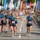 Cours relais entreprise: équipe TechCorp échangeant le témoin lors d’un marathon relais inter-entreprises sur ligne d’arrivée entourée de tribunes et spectateurs.