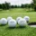 Balles de golf blanches autour d’un trou de départ sur parcours verdoyant, prêt à être jouées, avec les noms Callaway, Titleist et TaylorMade visibles. comment choisir sa balle de golf intégré naturellement.