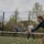 Quatre personnes jouent au tennis sur un court extérieur, deux près du filet et deux à l’arrière, en mouvement et concentrées.