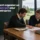 Deux hommes assis à une table en bois discutent devant des documents de travail et une tasse de café, lors d'une séance de