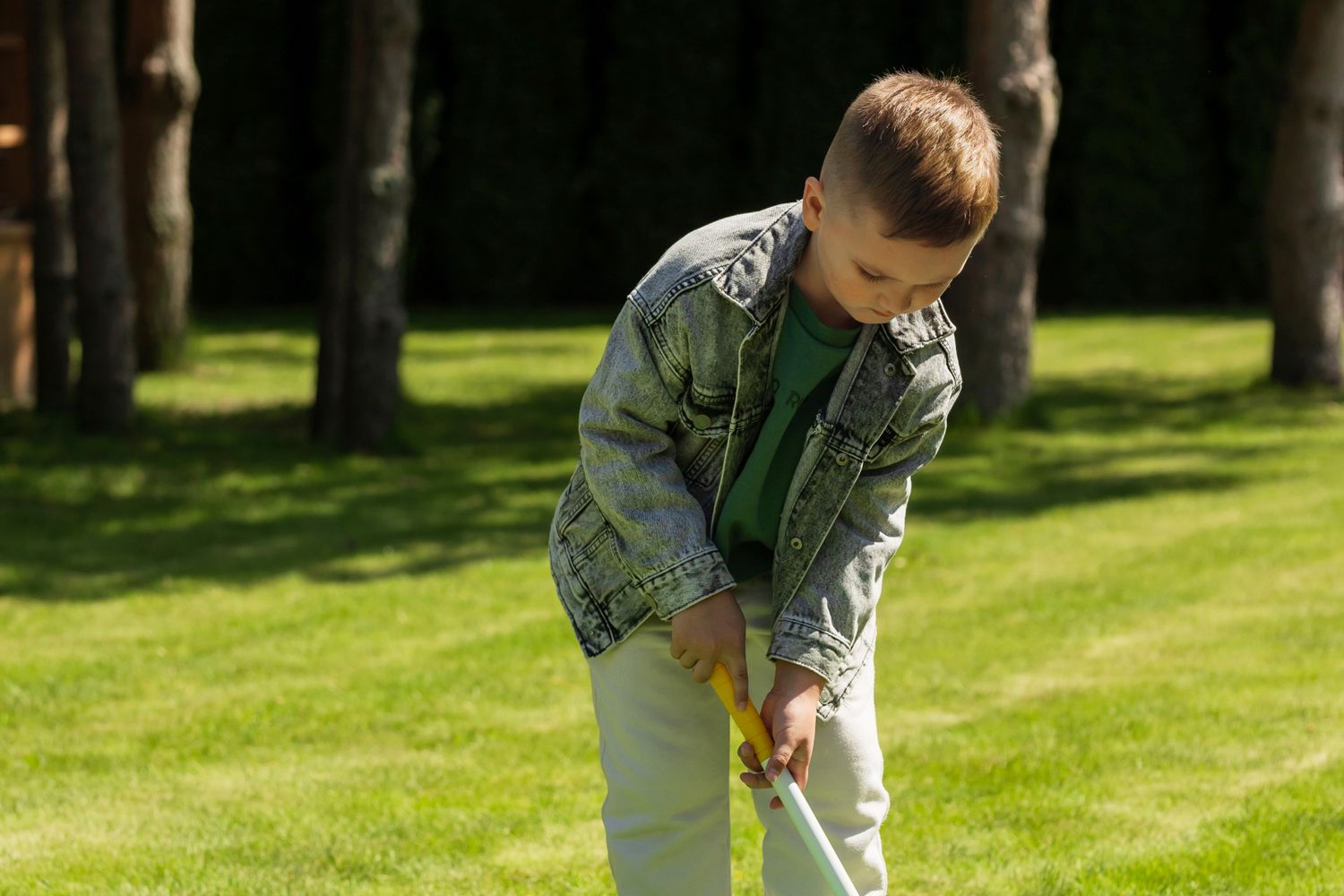 Un jeune garçon en chemise et denim tient un club de golf dans un parcours verdoyant.