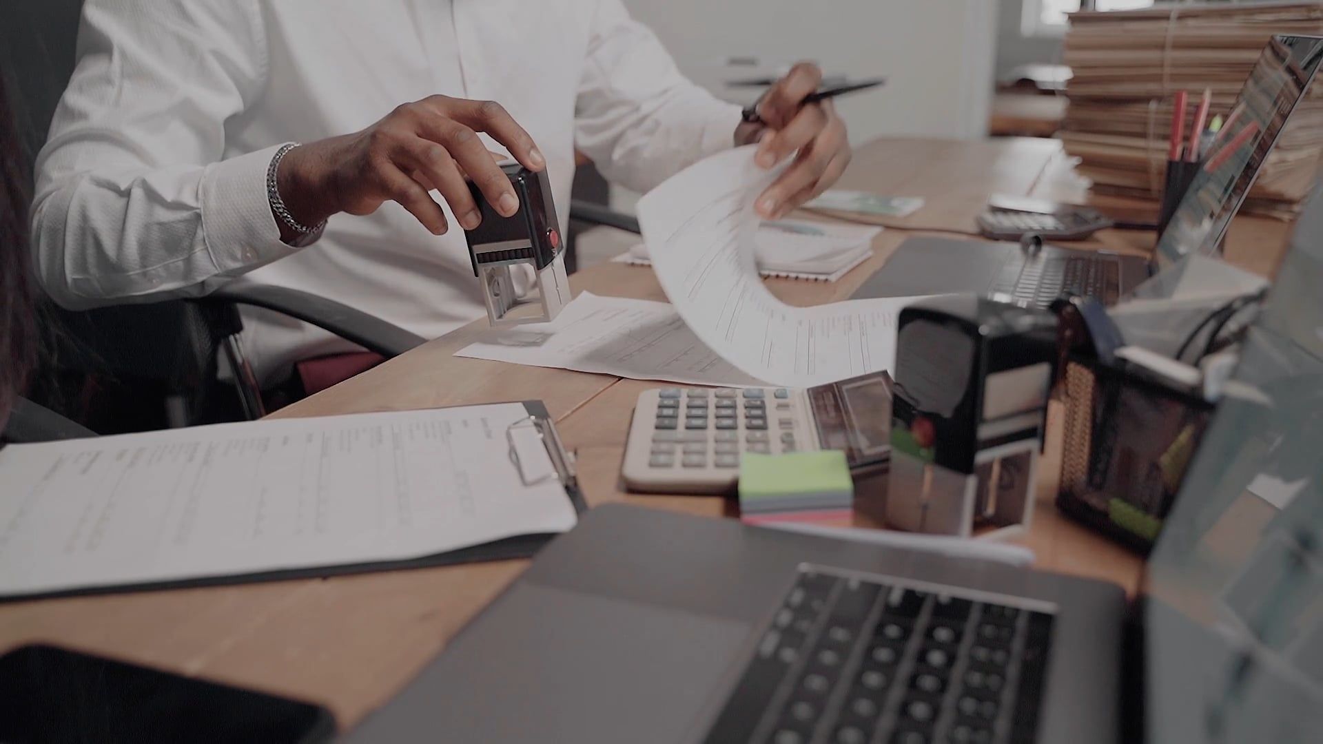 Personne au bureau en train de vérifier des documents et d’utiliser des outils de comptabilité sur le tas.